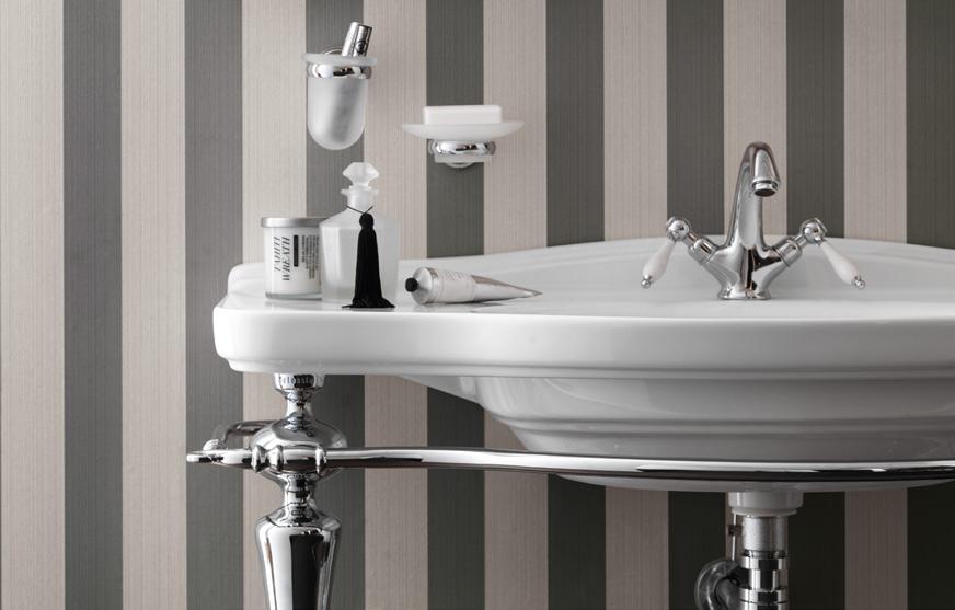 Bathroom sink with chrome faucet and accessories against striped wallpaper.