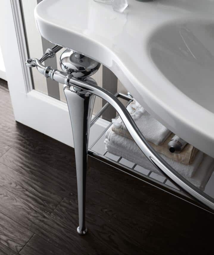 A white bathroom sink with chrome legs and towel storage underneath, set against a dark wood floor.
