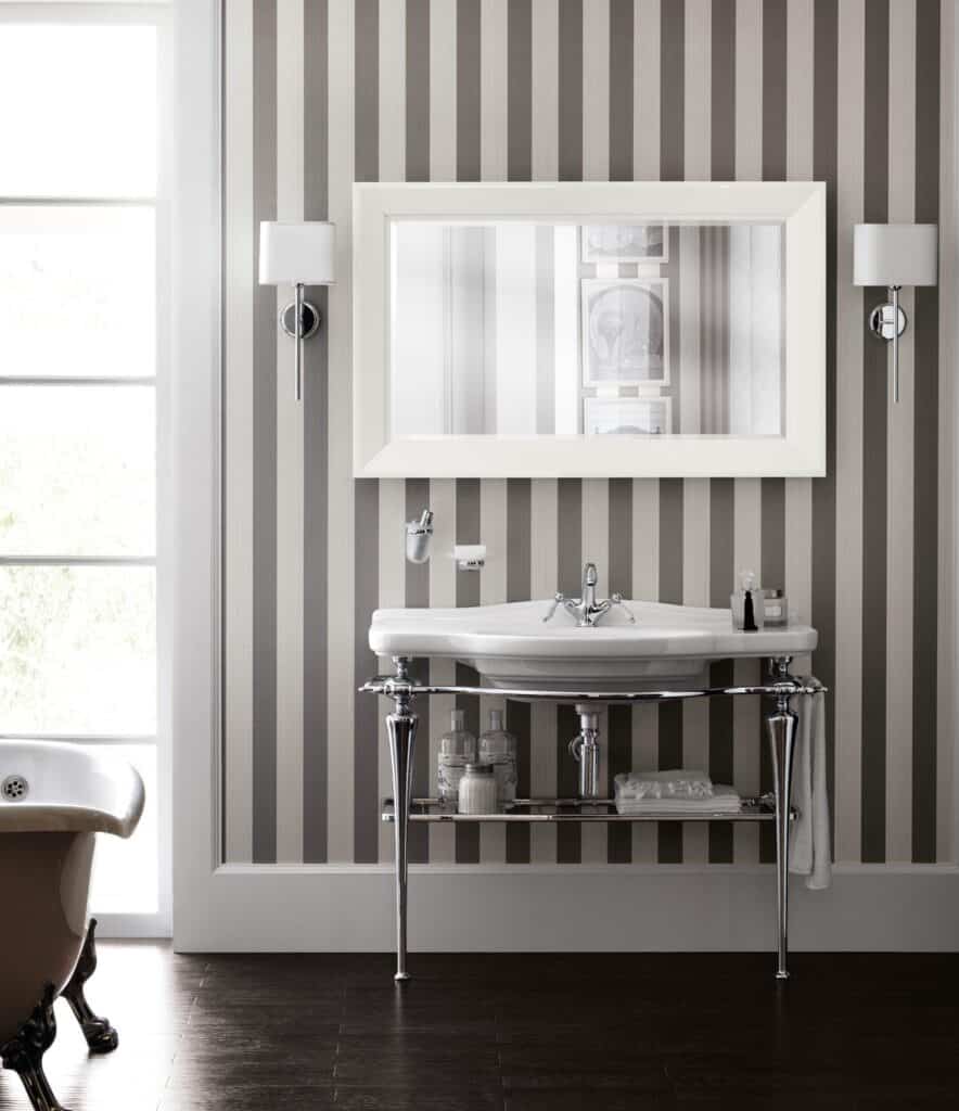 Classic bathroom with striped wallpaper, wall sconces, large mirror, vintage sink with metal legs, and a clawfoot tub.