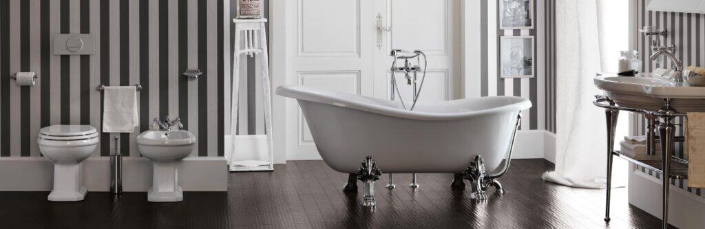 Elegant bathroom with a clawfoot bathtub, striped wallpaper, freestanding basin, bidet, and toilet on dark wood flooring.