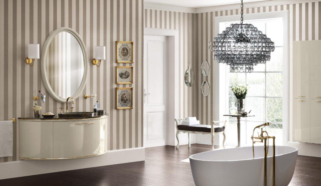 Elegant bathroom with striped wallpaper, oval mirror, chandelier, freestanding bathtub, and decorative stool.