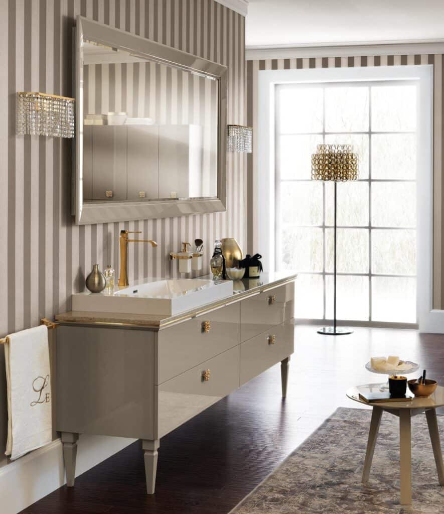 Elegant bathroom with a large mirror and striped wallpaper, featuring a long vanity with gold fixtures, modern decor items, and a large window.