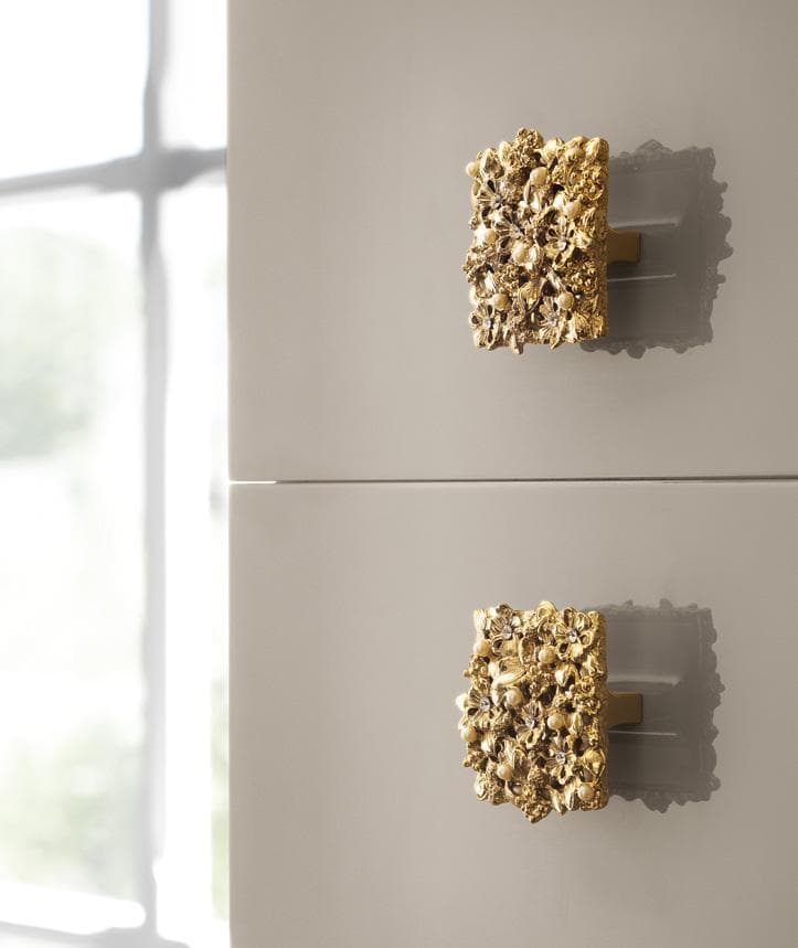 Ornate gold cabinet handles on a gray surface, with a window in the background.