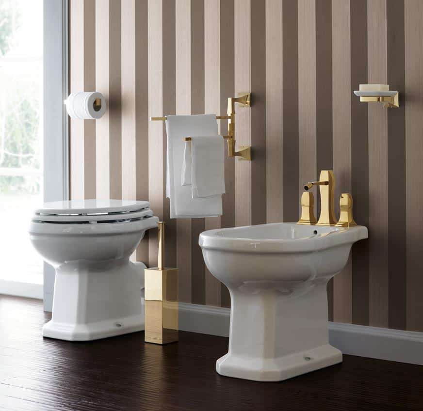 Luxurious bathroom with a striped wallpaper, featuring a toilet and bidet with gold fixtures, a gold toilet paper holder, and a matching toilet brush on a dark wood floor.