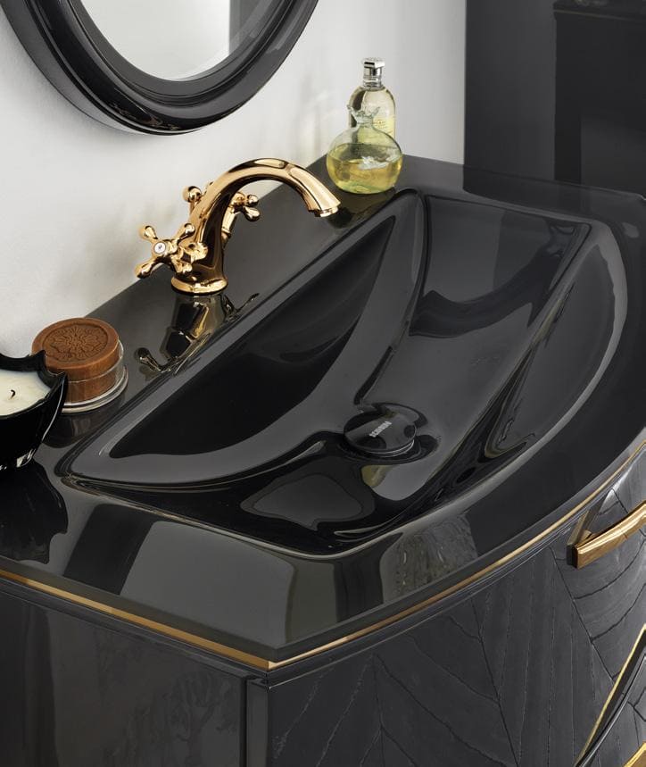 A luxurious black bathroom sink with a gold faucet and a round mirror above. A bottle of liquid soap, a small container, and a black dish are placed on the counter.