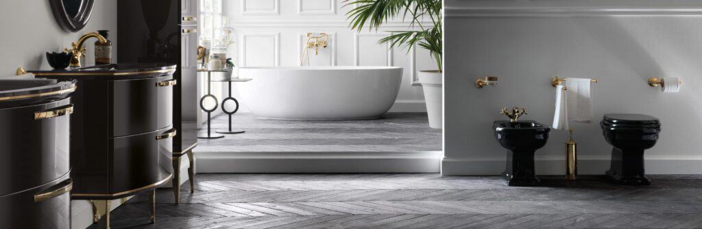 Luxurious bathroom with black fixtures, gold accents, a freestanding white bathtub, herringbone-patterned dark wood flooring, and decorative plants.
