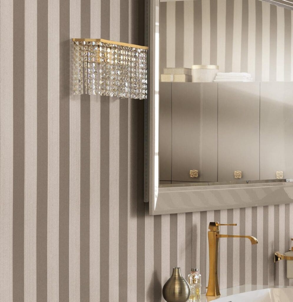 Luxurious bathroom with striped wallpaper, gold faucet, crystal wall light fixture, and a large mirror reflecting cabinets and towels.