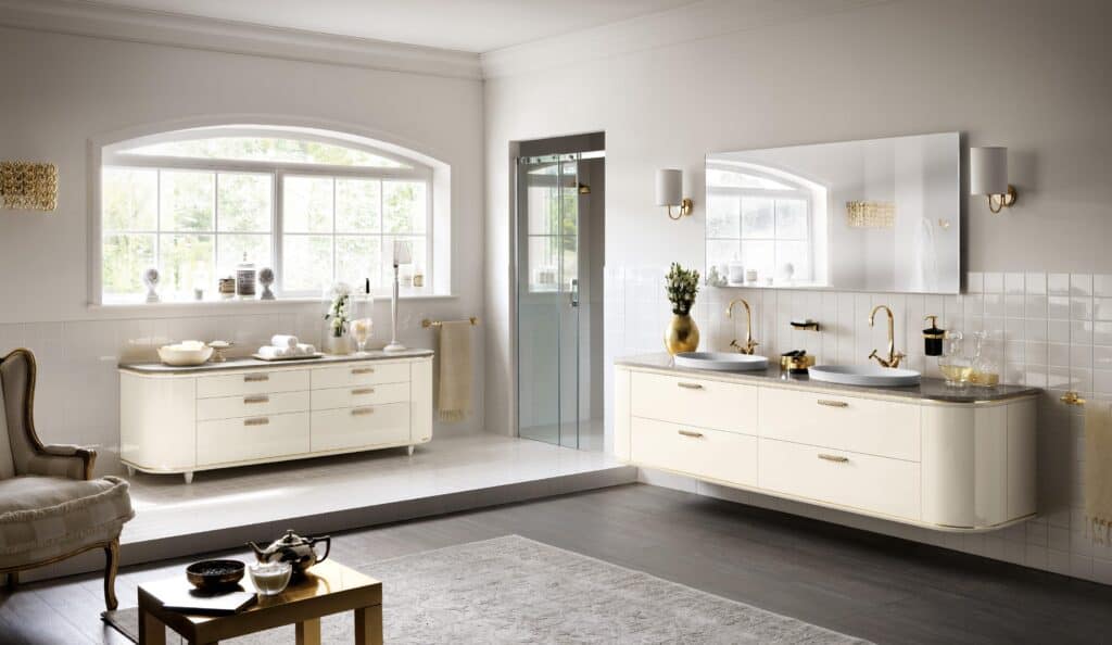 Elegant bathroom with cream cabinets, gold fixtures, double sinks, a large mirror, and natural lighting from a wide window.