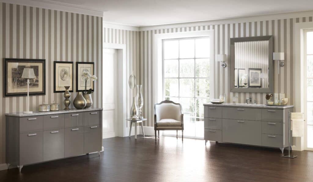 Elegant room with striped wallpaper, two stylish dressers, a large mirror, framed artwork, a cushioned chair, and a side table with decorative vases.