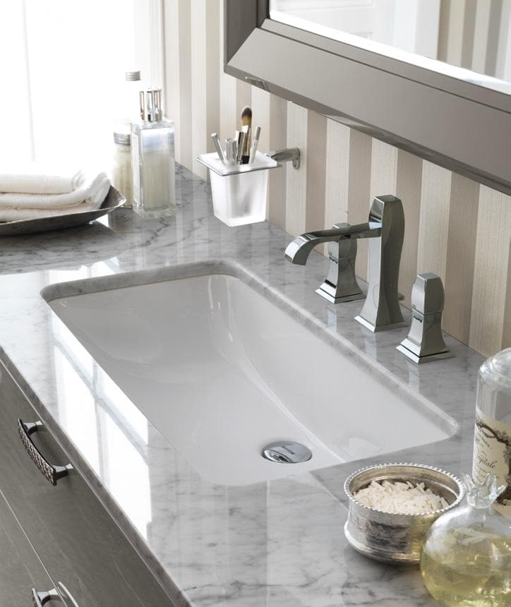 Modern bathroom vanity with a rectangular marble countertop, a built-in sink, sleek chrome faucets, and various toiletries neatly arranged.