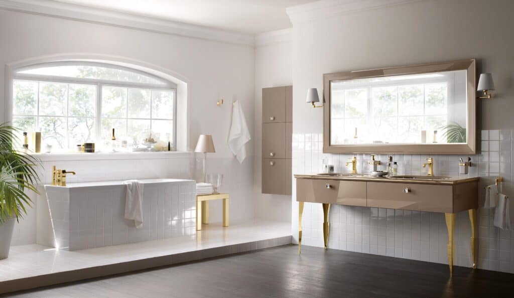 Luxurious bathroom with a large white bathtub, gold fixtures, dual sinks, a large framed mirror, and a window providing natural light.