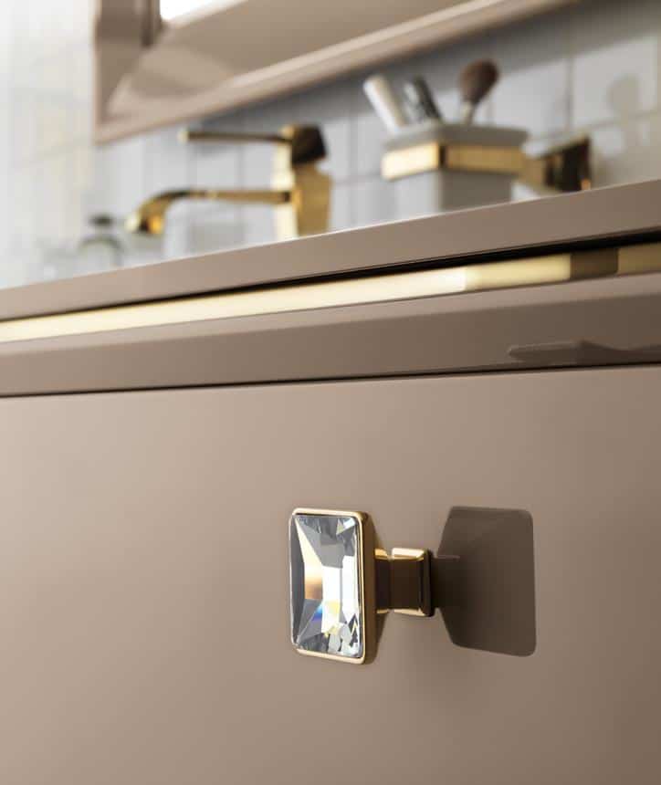 A close-up of a cabinet door with a square crystal knob and gold accents in a bathroom or kitchen setting.