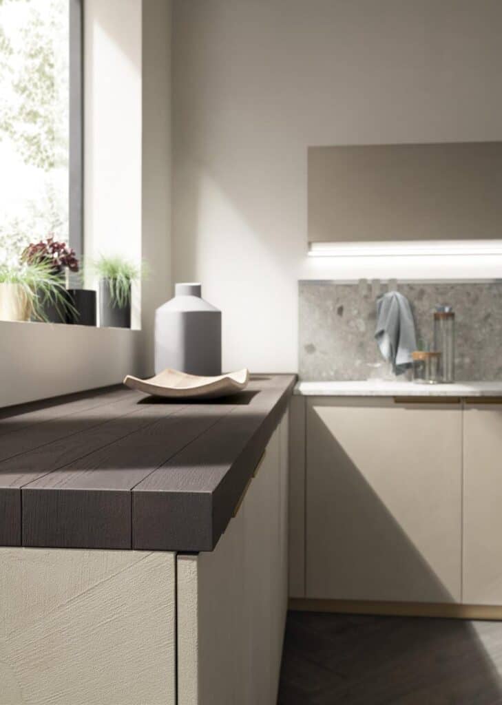 Modern kitchen interior with wood countertop, plants on the windowsill, and gray cabinets.