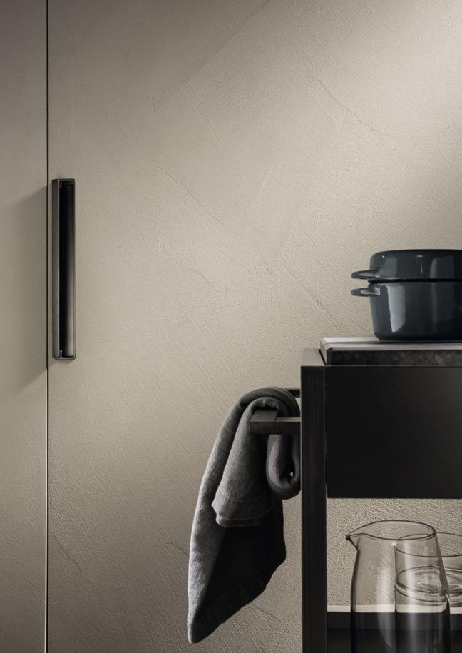 A minimalist kitchen scene with a textured wall, a black cabinet handle, a dark pot on a countertop, and a textured cloth hanging from a bar.
