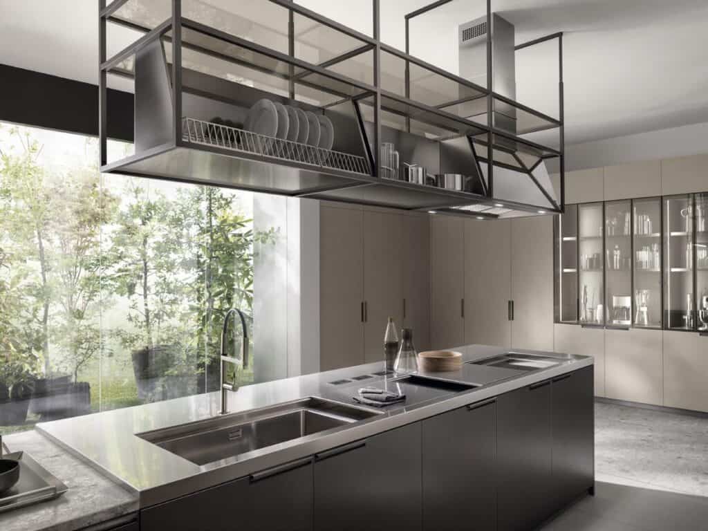 Modern kitchen with sleek countertops, a stainless steel sink, overhead metal shelving, large glass windows, and cabinetry.