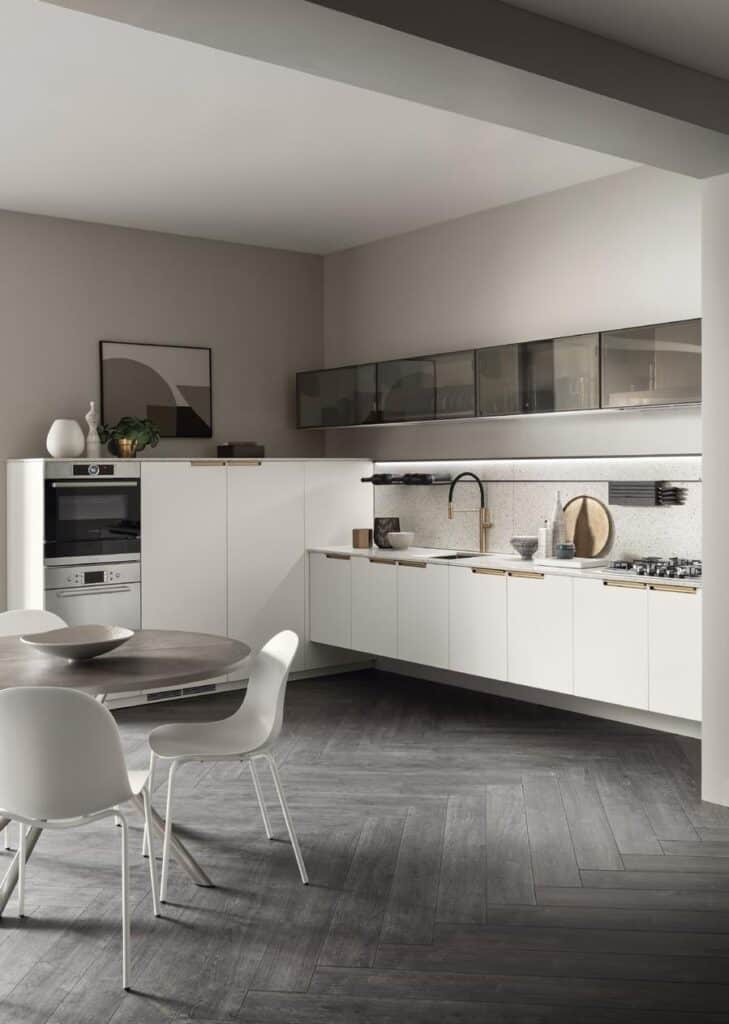 Modern kitchen with white cabinets, black countertop, integrated appliances, and gray herringbone floor, featuring a round dining table with white chairs.