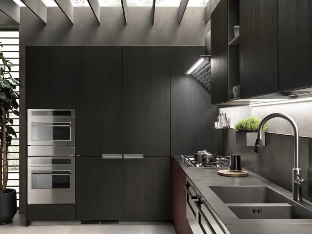 Modern kitchen with dark wood cabinets, stainless steel appliances, and a sleek countertop with a built-in sink and stove. A potted plant is visible in the corner.