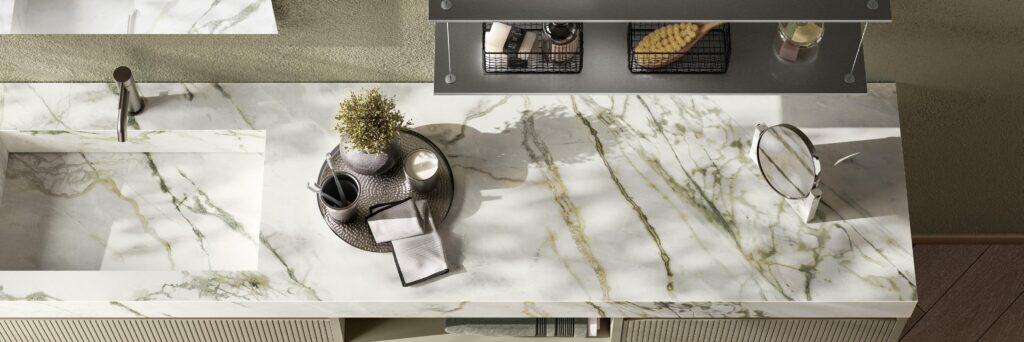 Marble countertop with a modern sink, faucet, a round tray holding a potted plant, cup, candle, and cloth, with a shelf above.