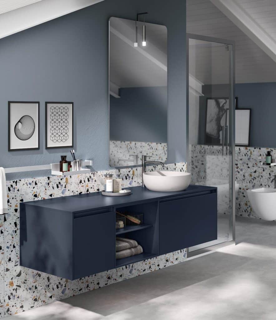 Modern bathroom with a blue floating vanity, terrazzo backsplash, large mirror, and minimalist decor under a sloped ceiling.