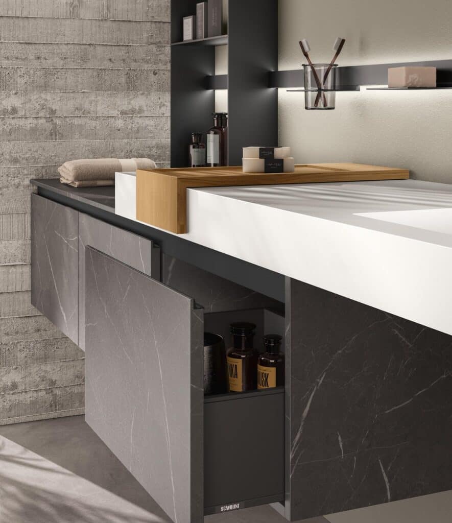 Modern bathroom vanity with a concrete-textured wall, featuring a dark marble cabinet, countertop accessories, and an open drawer with bottles.