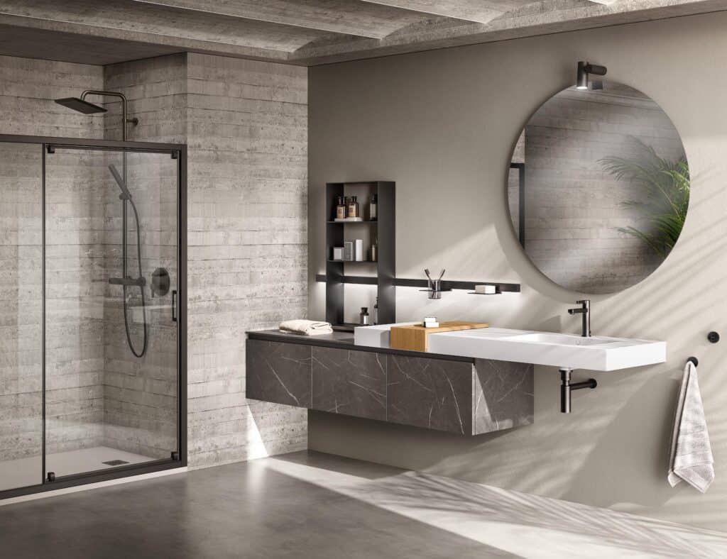 Modern bathroom with a concrete tile shower, glass door, wall-mounted sink, large round mirror, black shelving, and a gray towel on a hook.