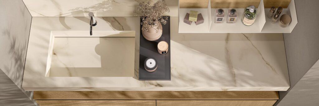 Marble bathroom countertop with integrated sink, faucet, decorative vase with dried flowers, and assorted toiletries on shelves.