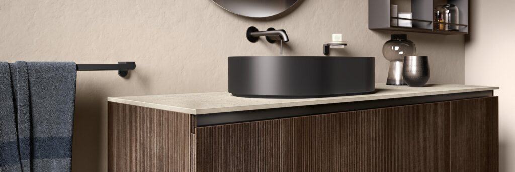 Modern bathroom with a textured dark wood vanity, black round vessel sink, wall-mounted faucet, gray towel, and shelves with decorative items.