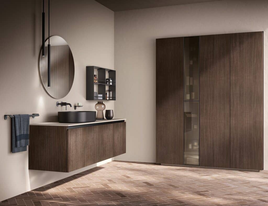 Modern bathroom with a round mirror, dark basin, wooden cabinetry, and a towel rack against a neutral-colored wall.