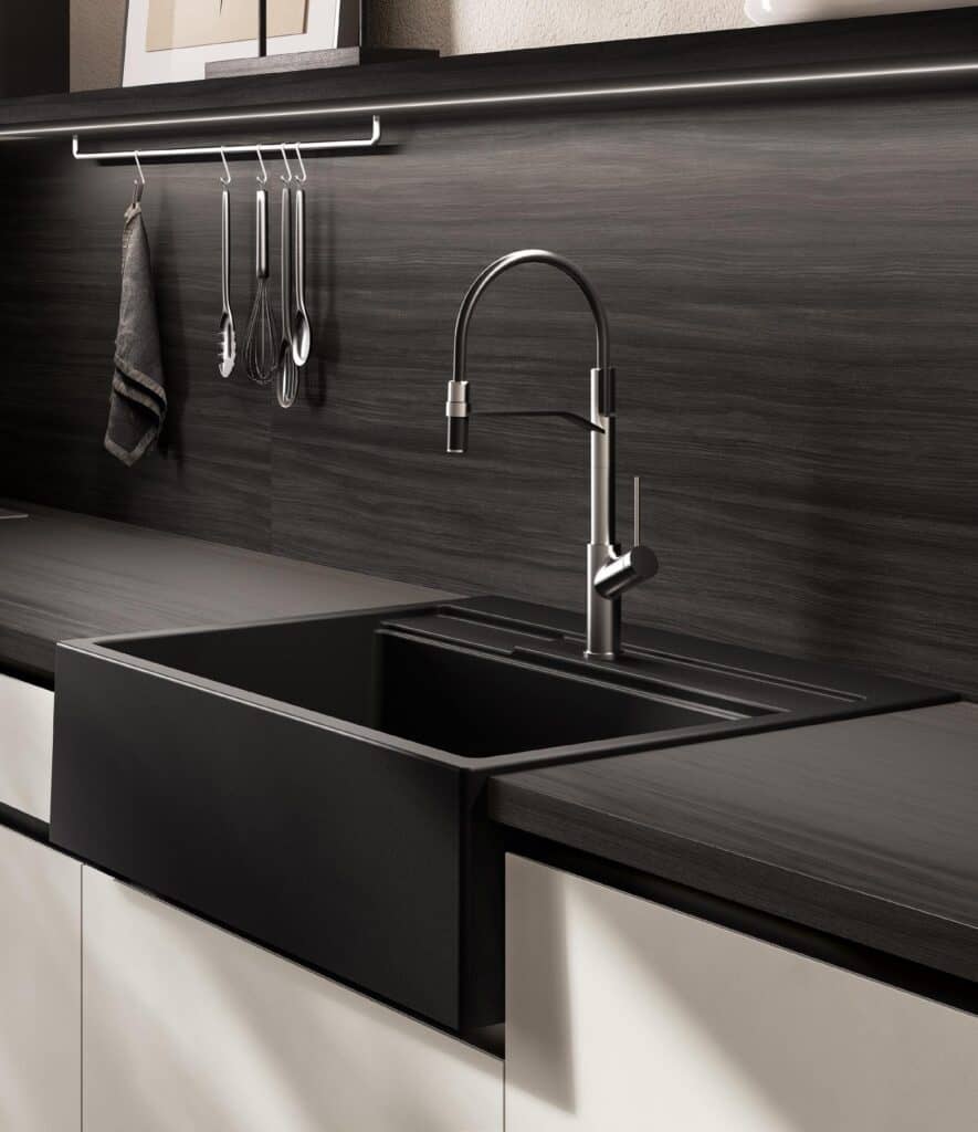 Modern kitchen sink with dark countertop, stainless steel faucet, and utensils hanging on a rail.