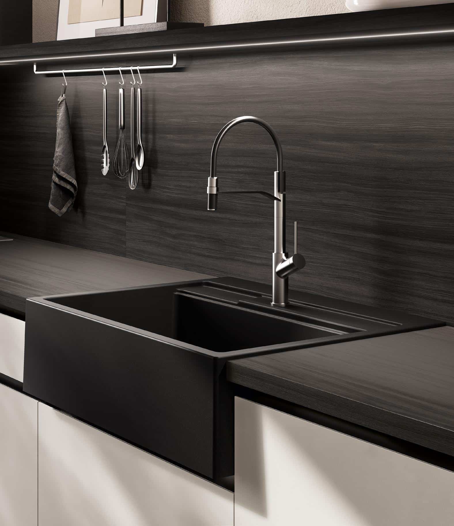 Modern kitchen sink with a tall, curved faucet, black countertop, and utensils hanging on a wall rail.