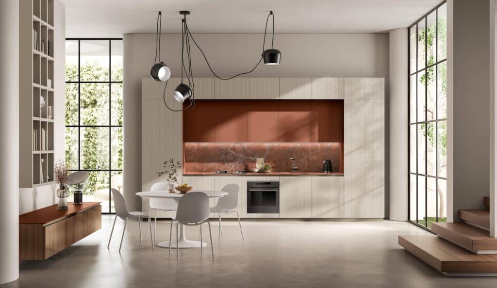 Modern kitchen with beige cabinets, red marble backsplash, a round dining table with white chairs, and large windows allowing natural light in.