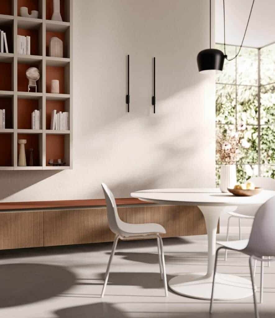Modern dining room with sleek white chairs, a round table, minimalistic pendant light, wooden cabinetry, and wall-mounted shelves with decorative items.