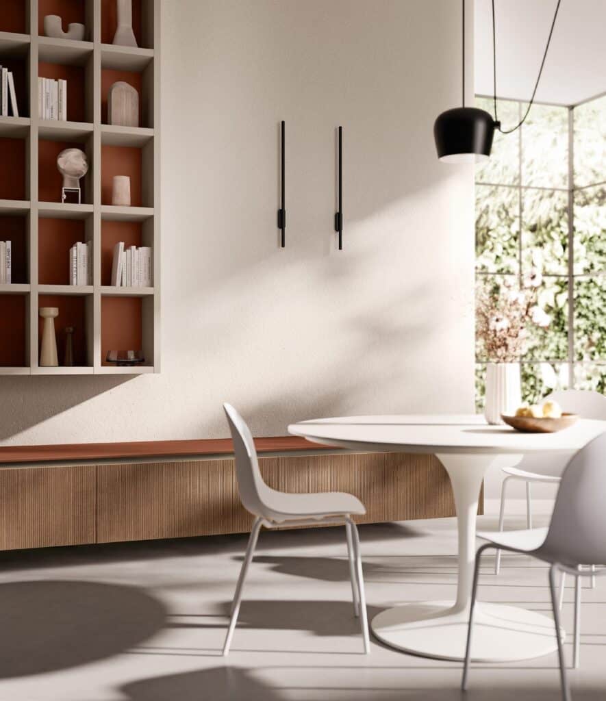 Modern dining area with a round white table, white chairs, built-in shelving with decorative items, and a large window providing natural light.