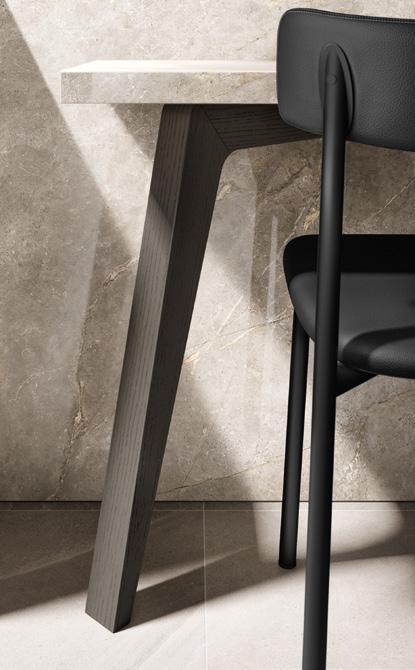 Photograph of a table with a slanted wooden leg and a black chair against a textured beige wall.