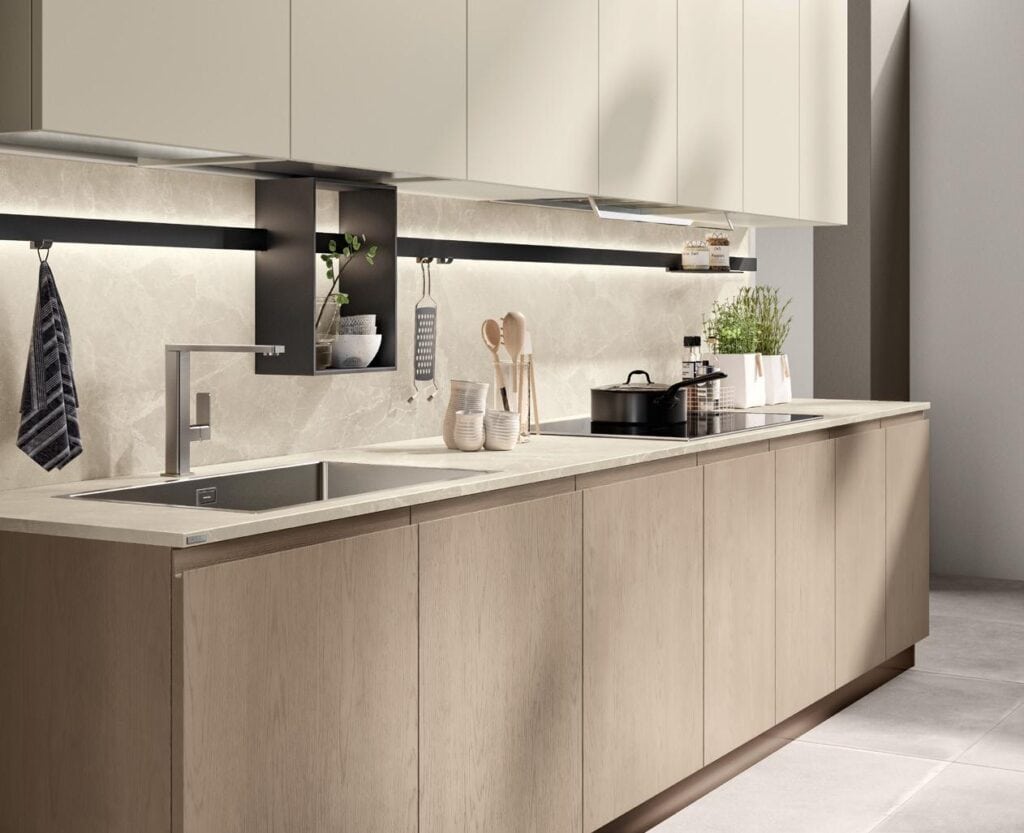 Modern kitchen with light wood cabinets, a stainless steel sink, and a minimalist design, featuring built-in shelves, a potted plant, and various kitchen utensils.