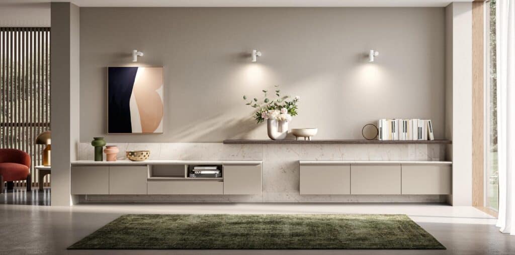 Modern living room with minimalist beige cabinets, abstract artwork, decorative vases, and a wall-mounted shelf with books, illuminated by wall sconces.
