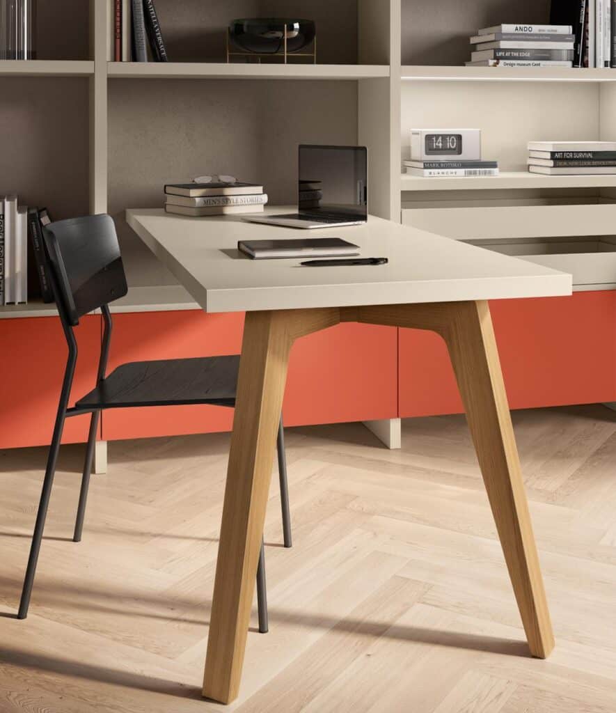 Workspace with a modern desk, black chair, laptop, and books on a light wooden floor with red cabinets in the background.