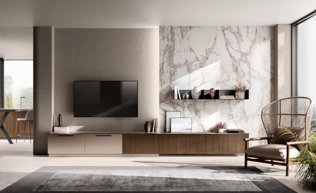 Modern living room with a wall-mounted flat-screen TV, marble accent wall, minimalist furniture including a low cabinet, wicker chair, and decorative items, with large windows providing natural light.