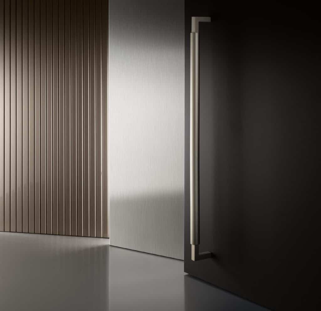 Modern interior with a sleek metal door handle, vertical paneling, and smooth reflective surfaces.