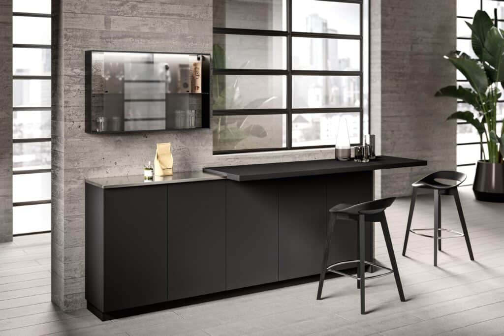 Modern kitchen interior with dark cabinets, a sleek countertop, two black bar stools, large windows, and a potted plant.