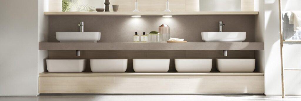 Modern bathroom with two vessel sinks, illuminated shelving, and storage compartments below.