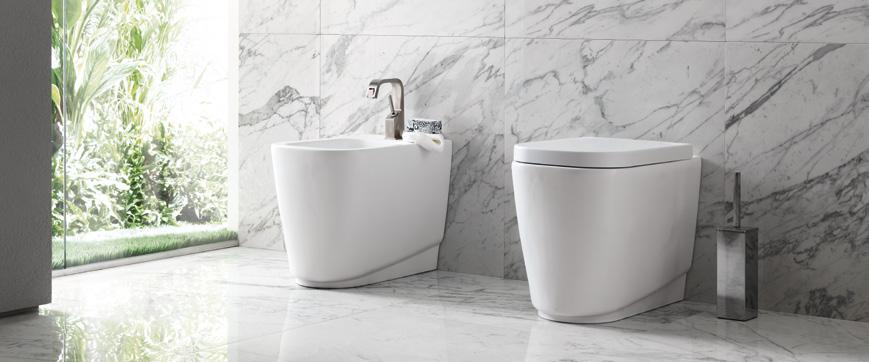 Modern bathroom with a white bidet and toilet, marble floor and walls, and a glass door leading to a garden.