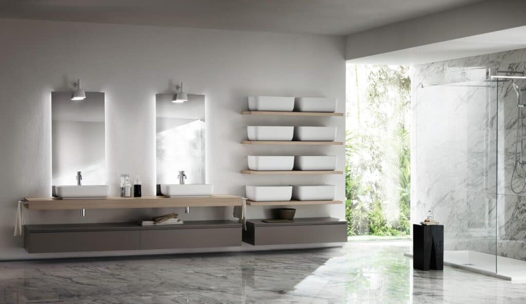 Modern bathroom with a double sink vanity, large mirrors, wall-mounted shelves with white containers, and a glass shower enclosure; features marble flooring and walls, with greenery visible through an open window.