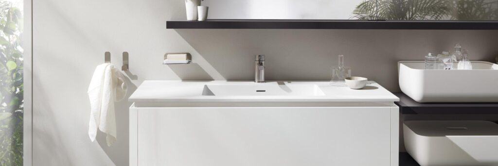 Modern bathroom sink with a sleek faucet, a towel on a hook, and a soap dish mounted on a light-colored wall.