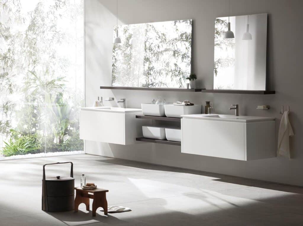 Modern bathroom with floating vanities, rectangular mirrors, and natural light from a large window overlooking greenery.