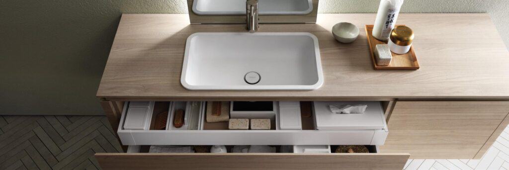 Modern bathroom vanity with a white sink, storage drawers, and toiletries on the countertop.