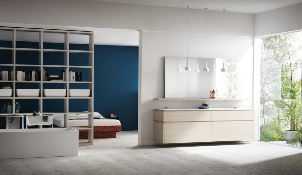 Modern open-concept interior with a living area, bookshelf partition, and minimalistic decor; large glass windows overlook greenery.