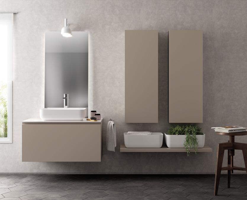 Modern bathroom with a floating vanity, large mirror, and a minimalist sink. Two tall cabinets are mounted on a textured wall. A shelf holds a basket and decorative greenery. A small stool with books is nearby, and a window brings in natural light.