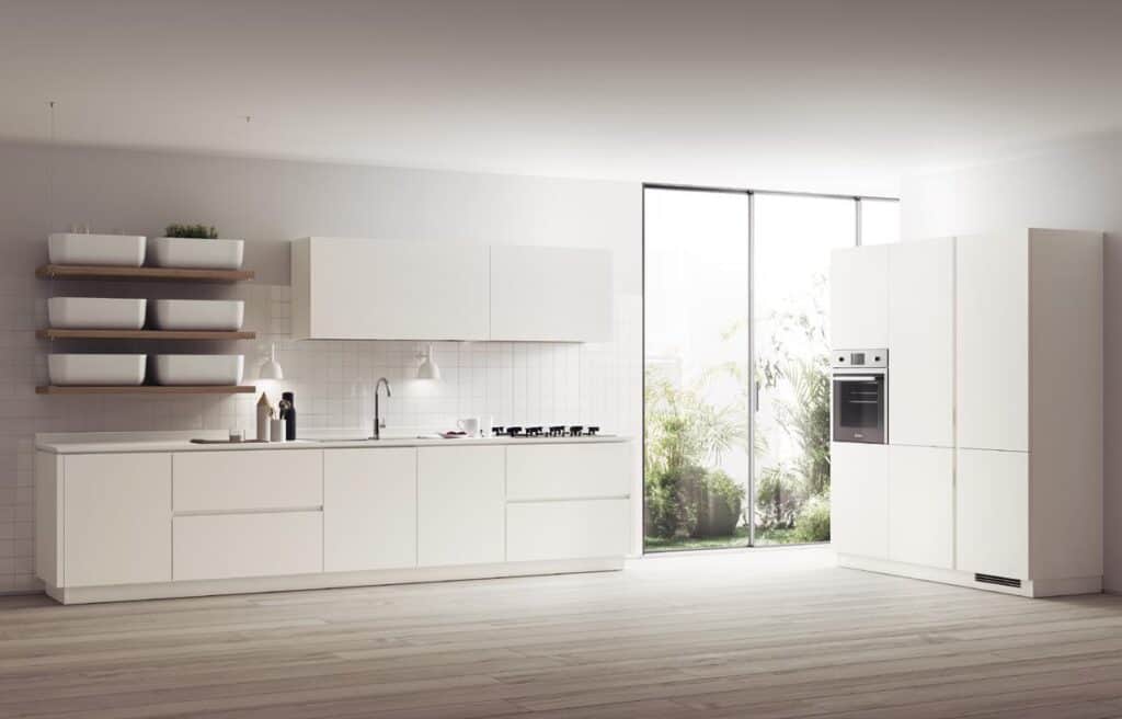 Modern kitchen with white cabinetry, minimalist design, a built-in oven, and open shelving, adjacent to a large window with greenery outside.