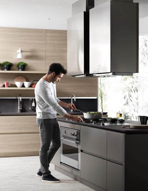 Man cooking in a modern kitchen with wooden and grey cabinets.